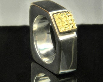 May include: A silver ring with a square-shaped gold top. The gold top has a textured pattern.