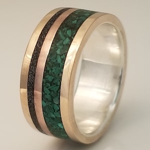 Könnte beinhalten: Ein silberner Ring mit einer grünen, schwarzen und roségoldenen Einlage. Die Einlage besteht aus Malachit, schwarzem Holz und Roségold.