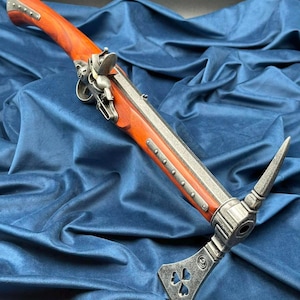 Op de afbeelding: Een replica van een combinatie wapen, met een houten handvat en een metalen loop. Het wapen heeft een pikhouweelkop en een trekker. Het houten handvat is roodbruin en de metalen onderdelen zijn zilver.