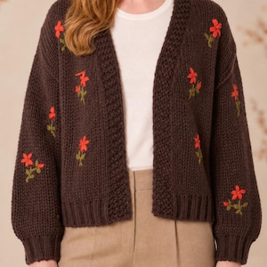 May include: A dark brown open-front knit cardigan featuring long sleeves and a ribbed trim along the collar and cuffs. The garment is decorated with small, embroidered red flowers with green stems scattered across the front and sleeves.