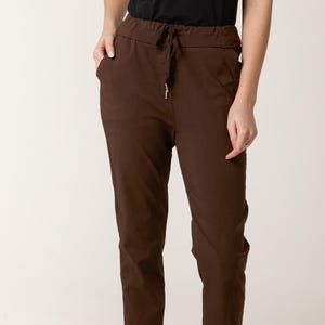 Op de afbeelding: Bruine vrijetijdsbroek met een tailleband met trekkoord en omgeslagen zomen. De broek heeft voorzakken en wordt gecombineerd met zwarte ballerina's. De stof lijkt een lichtgewicht materiaal te zijn, geschikt voor dagelijks gebruik.