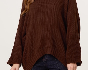 May include: A dark brown long-sleeve sweater featuring a wide scoop neckline, a textured waffle-knit pattern, and a high-low hemline with ribbed cuffs and a ribbed bottom edge, paired with dark blue denim jeans with a visible center seam.
