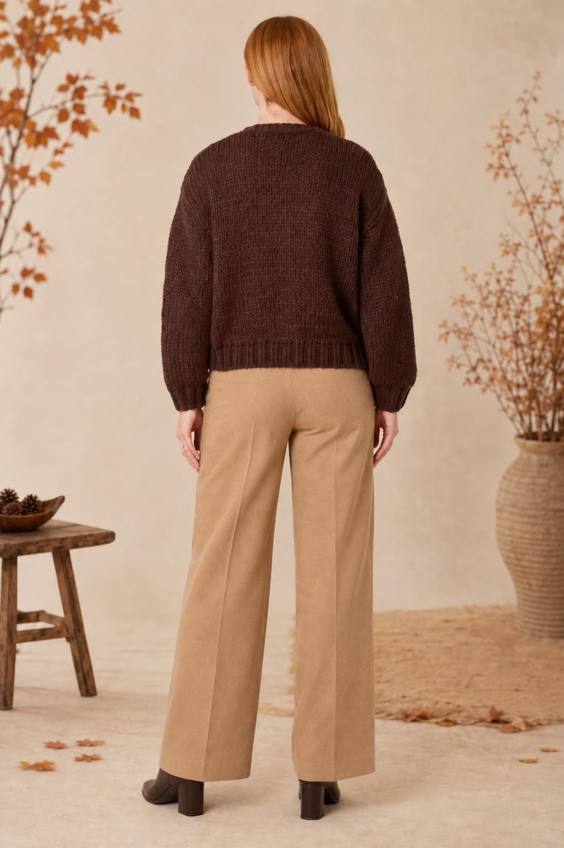 May include: A dark brown long-sleeved knit sweater with a ribbed crew neckline, cuffs, and hem, paired with tan wide-leg trousers featuring a pressed crease down the center of each leg and black block-heeled ankle boots.