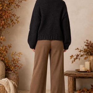 May include: A black long-sleeved knit sweater with a ribbed crew neckline and hem, paired with solid brown wide-leg trousers. The sweater features a textured knit pattern and the trousers have a straight, loose fit reaching the ankles.
