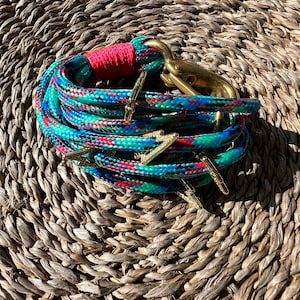 May include: A colorful rope bracelet with a brass clasp and gold lightning bolt charms. The bracelet is on a woven straw background.