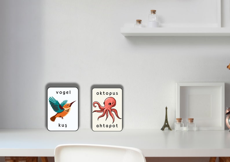 May include: Two flashcards with illustrations and words in German and Turkish. The first card shows a blue and orange bird with the words "vogel" and "kuş". The second card shows a pink octopus with the words "oktopus" and "ahtapot".