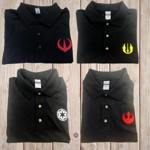 May include: Four black polo shirts with different embroidered logos. The logos are red, yellow, white, and red. The shirts are folded and laid out on a wooden surface.