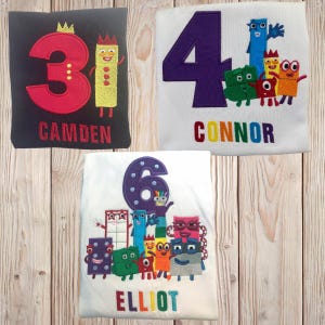 May include: Three personalized t-shirts featuring the characters from the show 'Numberblocks'. The first shirt is black with a red number 3 and the name 'CAMDEN' in red. The second shirt is white with a purple number 4 and the name 'CONNOR' in rainbow colors. The third shirt is white with a purple number 6 and the name 'ELLIOT' in rainbow colors.