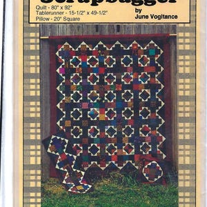 May include: A quilting pattern titled "Scrapbagger" by June Vogitance. The pattern includes instructions for a quilt, table runner, and pillow. The quilt is shown in the image, featuring a patchwork design with black, red, and white squares.