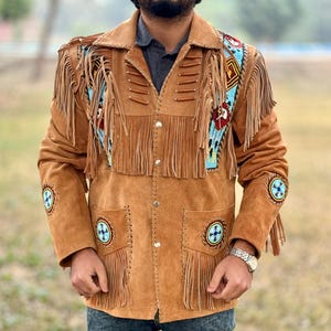 May include: A brown suede jacket with fringe and beaded details. The jacket has a button-up front and long sleeves. The beading is in a geometric pattern and includes blue, red, and white beads.