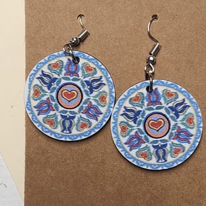 May include: A pair of round wooden earrings with a blue, white, red, and orange floral pattern. The earrings have silver hooks.