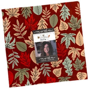 May include: A square fabric swatch featuring a deep red background with a repeating pattern of autumn leaves in shades of light green, cream, and red. A Moda Windfall label with a 4-inch ruler is placed on top of the fabric, showing the brand name.