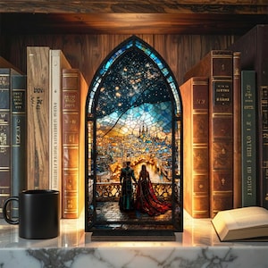 May include: A stained glass panel depicting a couple overlooking a cityscape at sunset. The panel is framed in black and set on a wooden base. The background features a shelf with antique books and a black mug.