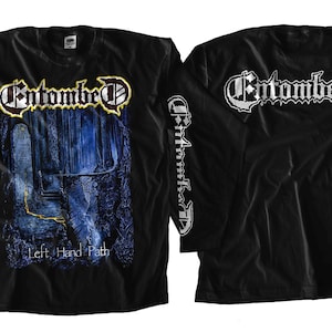 Puede incluir: Camiseta negra de manga larga con un estampado gráfico de una banda llamada "Entombed" y el texto "Left Hand Path". El nombre de la banda también está impreso en la parte posterior de la camiseta.