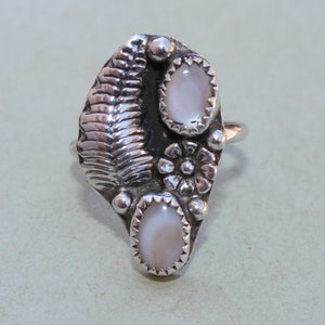 May include: A silver ring with two white opal stones set in a floral design. The ring is made in a leaf shape.