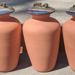 Puede incluir: Tres jarras de cer&aacute;mica color terracota con tapas a juego. Las tapas presentan tonos azules, morados y verdes. Cada jarra tiene un cuerpo redondeado y un cuello estrecho, ideal para la decoraci&oacute;n del hogar.