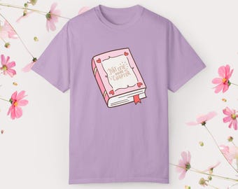 May include: A lavender t-shirt with a pink book graphic. The book has a heart border and the text "Just one more chapter" in gold lettering.
