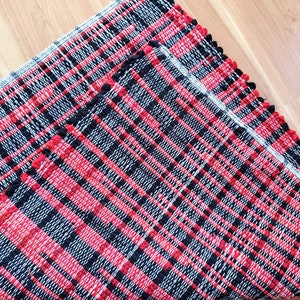 May include: Two red and black woven rugs with a white fringe border. The rugs are made of a thick, textured material and have a checkered pattern.