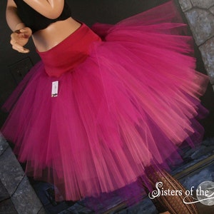 May include: A pink and purple ombre tulle skirt with a red waistband. The skirt is full and flowing, and it would be perfect for a party or special occasion.