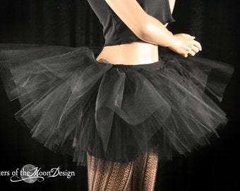 May include: A black tulle tutu skirt with multiple layers. The skirt is worn by a mannequin and is shown from the side.