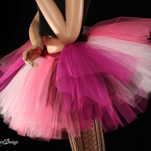 May include: A multi-layered tulle skirt in shades of pink, white, and burgundy. The skirt is full and fluffy, with a layered design.