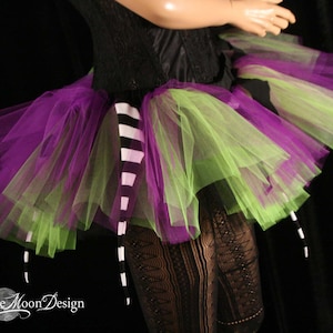 May include: A green and purple tulle tutu with a black and white striped tail. The tutu is layered and has a ruffled edge.