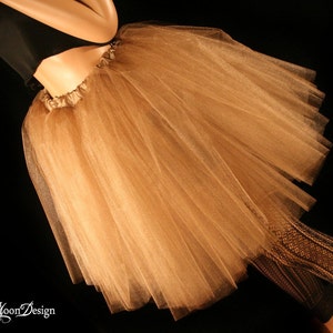 May include: A light brown tulle skirt with a gathered waistband. The skirt is layered and has a soft, flowing texture.