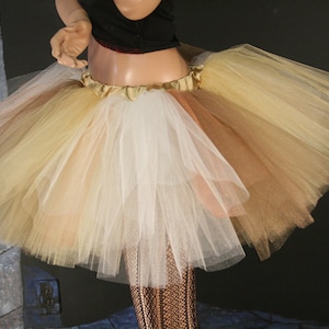 May include: A multi-layered tulle skirt in shades of beige, white, and brown. The skirt is gathered at the waist and has a satin waistband.