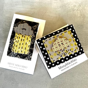 May include: Two handmade fabric brooches featuring a cloud design with a button centre. The brooches are displayed on white cards with black polka dots and the text "MissyMaoMao Handmade in Australia".
