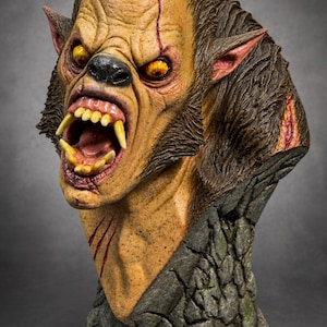 May include: A detailed werewolf bust featuring textured brown fur, yellow eyes, and an open mouth with sharp teeth. The creature has visible scars on its face and neck, and the base is sculpted to resemble dark, weathered stone blocks.
