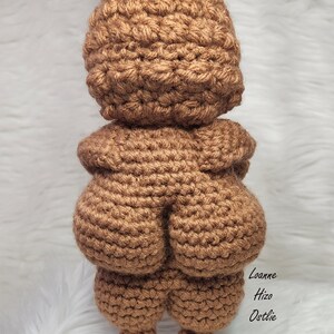 May include: A brown crocheted amigurumi doll with a round head and a large, round body. The doll has two small, round feet.