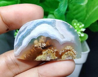 May include: A white and brown agate cabochon with a layered pattern. The agate has a translucent appearance with white, brown, and pink layers.