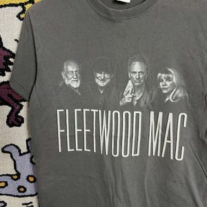 May include: A grey t-shirt with a black and white image of Fleetwood Mac. The band members are shown in a row, with the band's name printed in large white letters below the image.