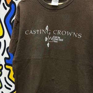 May include: Brown t-shirt with a white graphic of the band Casting Crowns. The graphic includes the band's name, a crown, and the text "Until the Whole World Hears".