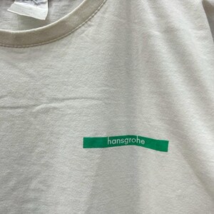 May include: White t-shirt with a green rectangular label that says "hansgrohe" on it.