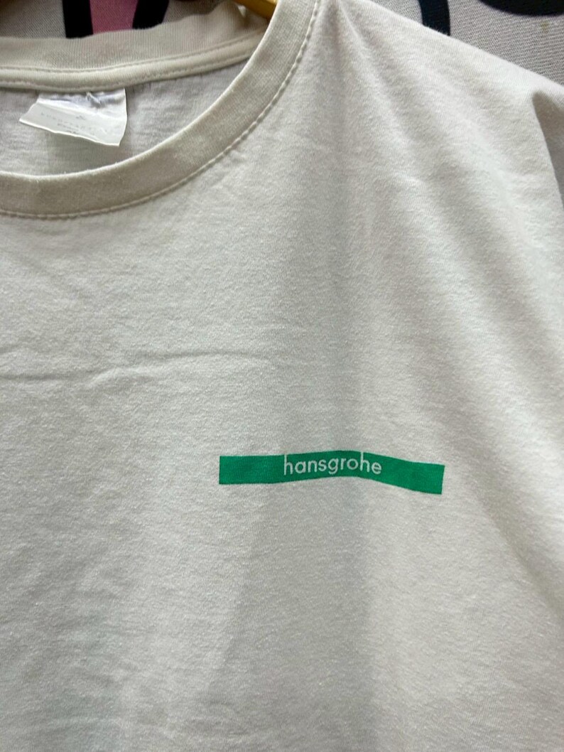 May include: White t-shirt with a green rectangular label that says "hansgrohe" on it.