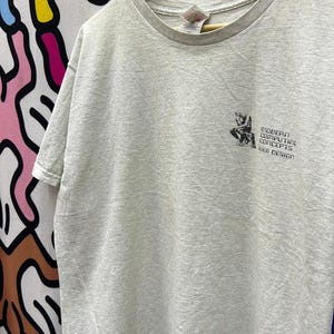 Puede incluir: Una camiseta gris claro con un gráfico de una persona sentada y el texto "MODERN COMPUTING CONCEPTS WEB DESIGN".