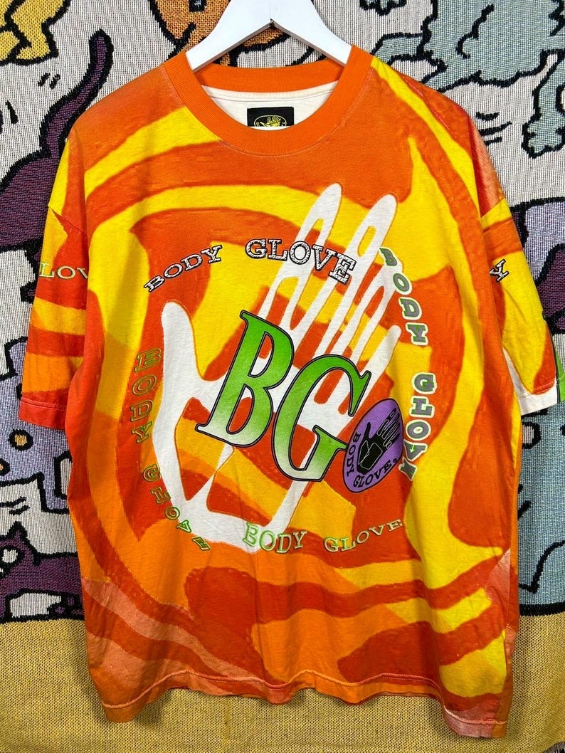 May include: Orange and yellow Body Glove t-shirt with a large white handprint graphic. The shirt features the text "BODY GLOVE" in a circular pattern around the handprint and "BG" in green letters. The shirt has a crew neck and short sleeves.