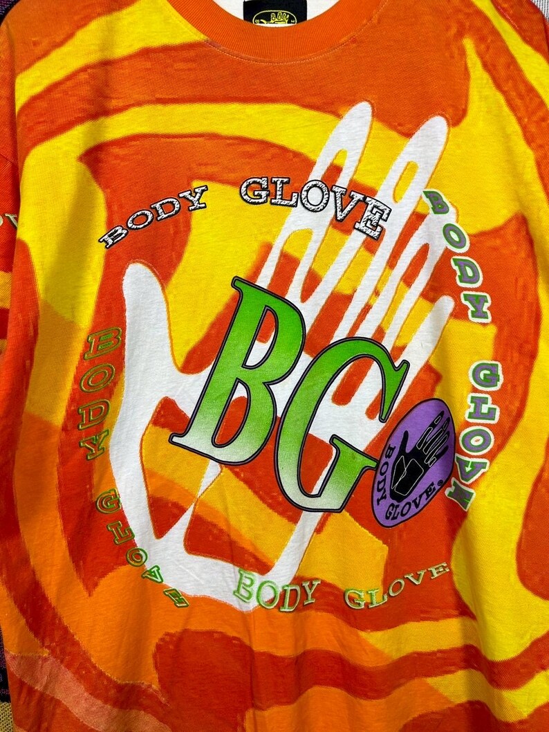May include: A long-sleeved shirt with a vibrant orange, yellow, and white tie-dye pattern. The shirt features the words "BODY GLOVE" in a circular design around a white handprint and the letters "BG" in green.