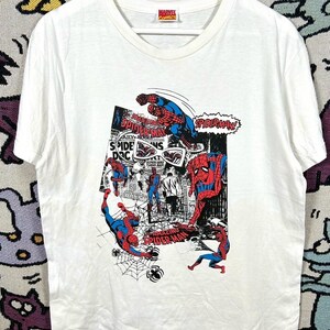 May include: White t-shirt featuring a comic book style graphic of Spider-Man in action poses. The design includes the words "Spider-Man" and "Marvel Comics". The shirt is hanging on a white hanger.