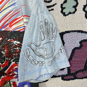 Puede incluir: Camiseta azul claro con un dise&ntilde;o gr&aacute;fico colorido. La manga presenta un contorno blanco de una mano con las palabras "BODY GLOVE" en un dise&ntilde;o circular. La camiseta tiene un aspecto vintage y desgastado.