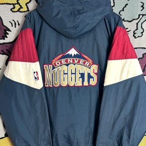 May include: A navy blue Denver Nuggets jacket with a hood. The jacket features red and white accents on the sleeves and the team's logo on the back. The Starter logo is visible on the lower left.