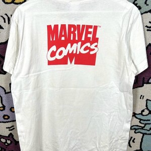 May include: White t-shirt featuring the Marvel Comics logo in red and white. The logo is centered on the back of the shirt. The shirt is hanging on a white hanger.