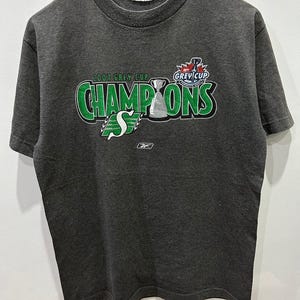 May include: A dark grey t-shirt with a green and white graphic print that says "2007 Grey Cup Champions" with a hockey trophy and the text "Grey Cup" in a smaller font.