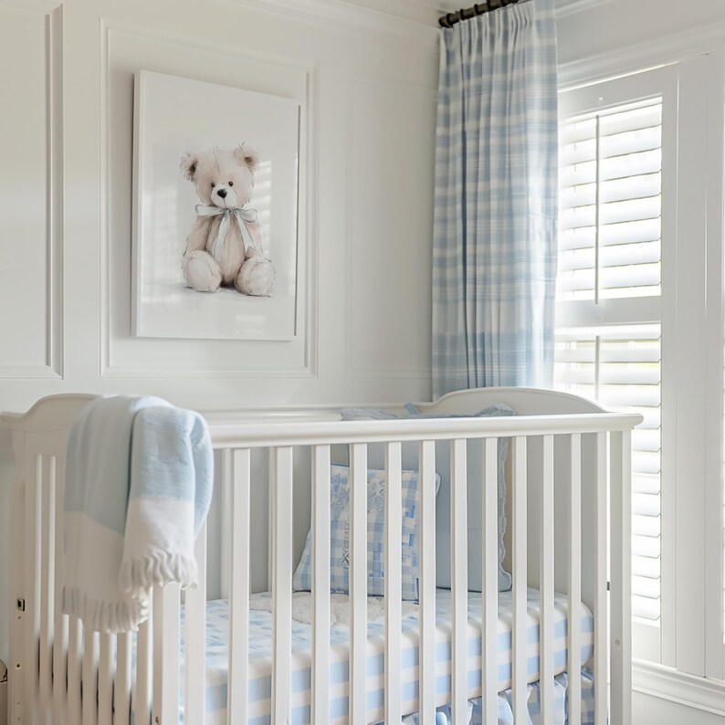 May include: A white cot with blue and white checked bedding and a matching blanket. A framed watercolour print of a teddy bear hangs above the cot. Blue and white plaid curtains and a window with shutters are visible.