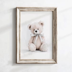 May include: A framed print showing a watercolour illustration of a teddy bear. The bear is light brown with a white bow. The frame is light, distressed wood. The artwork is set against a white background.