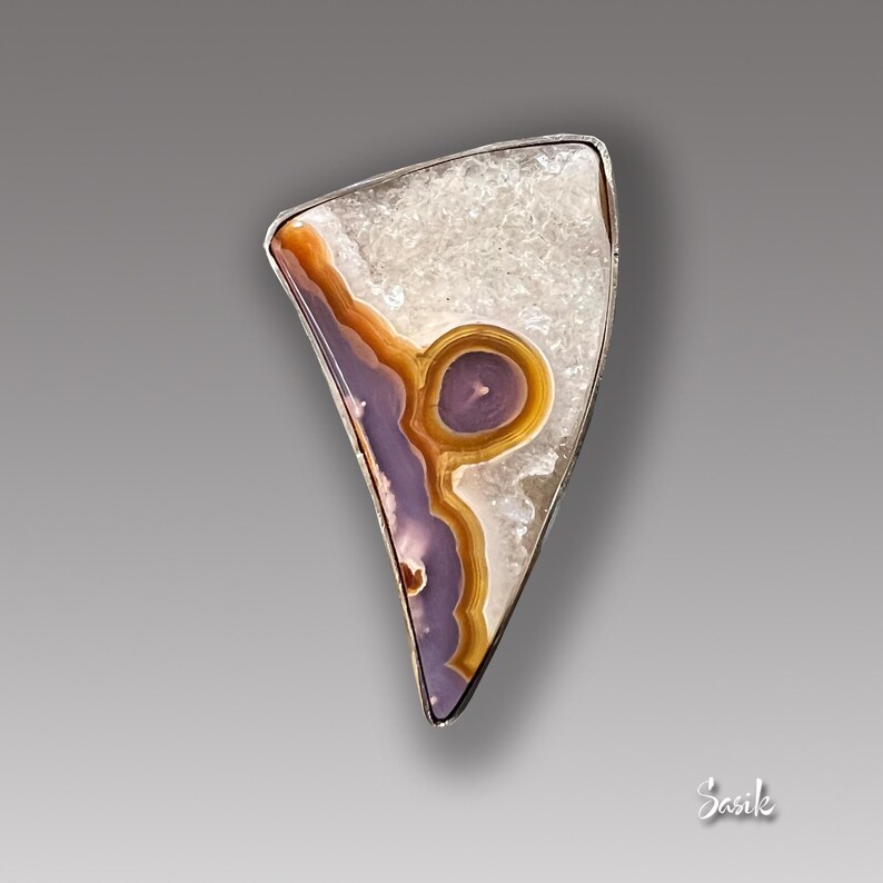 May include: A silver pendant featuring a unique, irregularly shaped agate stone with a purple and orange pattern. The stone is set in a silver bezel and has a white, crystalline background.