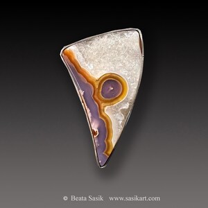 May include: A silver pendant featuring a triangular piece of agate with a purple, orange, and white pattern. The agate is set in a silver frame.
