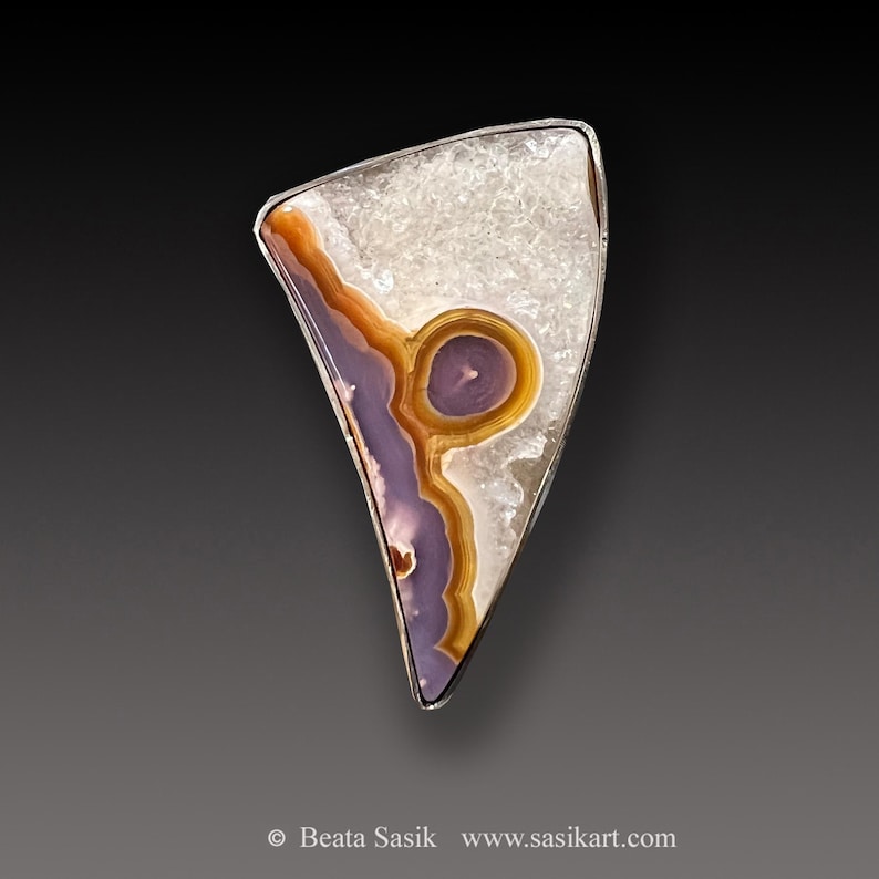 May include: A silver pendant featuring a triangular piece of agate with a purple, orange, and white pattern. The agate is set in a silver frame.