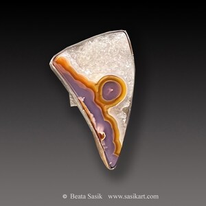 May include: A silver ring featuring a purple, orange and white agate stone. The stone is set in a triangular shape and displays a distinctive pattern.